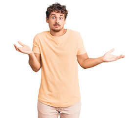 Young handsome man with curly hair wearing casual clothes clueless and confused expression with...