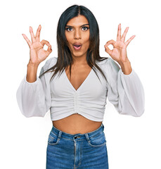 Young latin transsexual transgender woman wearing casual clothes looking surprised and shocked doing ok approval symbol with fingers. crazy expression