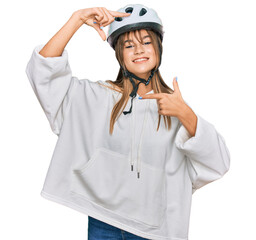 Teenager caucasian girl wearing bike helmet smiling making frame with hands and fingers with happy face. creativity and photography concept.