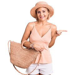 Young blonde woman wearing summer hat holding bag smiling happy pointing with hand and finger to...