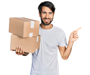 Hispanic man with blue eyes holding packages smiling happy pointing with hand and finger to the side