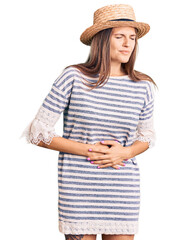 Beautiful caucasian woman wearing summer hat with hand on stomach because indigestion, painful illness feeling unwell. ache concept.
