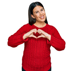 Beautiful brunette woman wearing casual sweater smiling in love showing heart symbol and shape with...