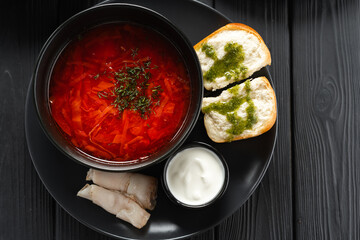 Top view of Ukrainian borscht red soup with garlic buns close-up in a bowl on the black wooden background