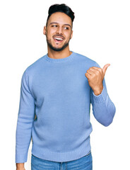 Young arab man wearing casual clothes smiling with happy face looking and pointing to the side with thumb up.