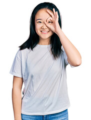 Obraz na płótnie Canvas Young chinese woman wearing casual white t shirt doing ok gesture with hand smiling, eye looking through fingers with happy face.