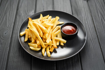 Plate with tasty golden french fries and ketchup on dark wooden background, top view