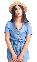 Brunette teenager girl wearing summer hat making fish face with lips, crazy and comical gesture. funny expression.