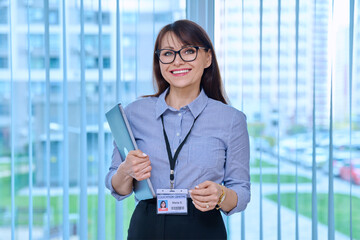 Middle aged woman with educational center id card badge, in office near window