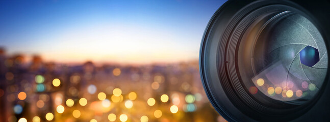 The camera lens on the background of the fiery city lights. Concept on the topic of news, media,...