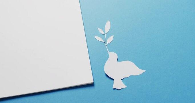 Close up of white dove with leaf, white paper and copy space on blue background