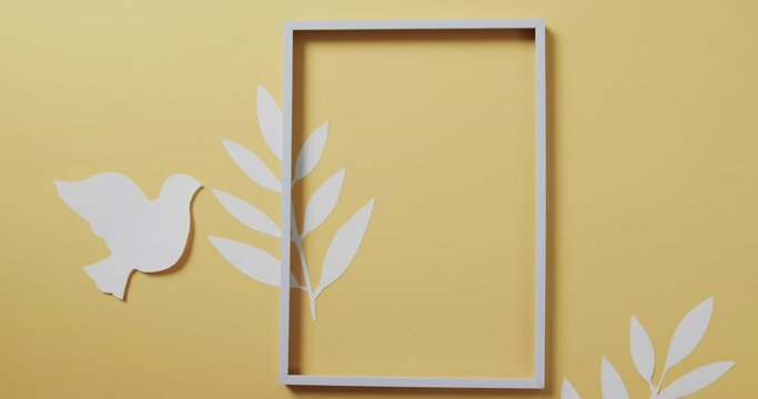 Close up of white dove with frame and leaves and copy space on yellow background
