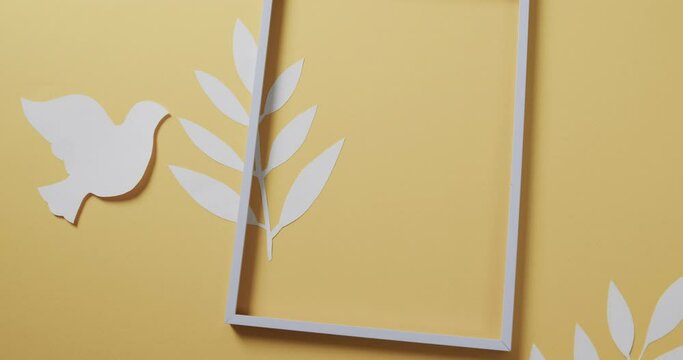 Close up of white dove with frame and leaves and copy space on yellow background