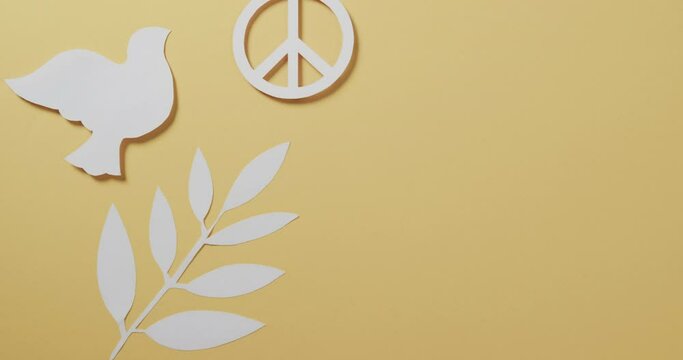 Close up of white dove with peace sign and leaf and copy space on yellow background