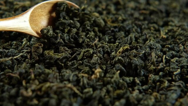 Black Dry Tea Wallpaper. Wooden spoon picks up Mix Black and Green Tea Leaves. Close Up, Macro. Top View. Texture. Copy Space. Dried Tea is Spinning, Rotating on Turntable. Food and Drink Background