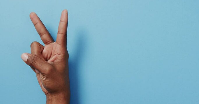 Close up of hand of biracial man showing peace sign with copy space on blue background