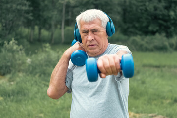 Naklejka premium Senior man working out outdoors. Person lifting dumbbells. Old male exercising at park. Healthy people lifestyle. Active sport training. Older elderly sportsman doing fitness exercise. Workout session