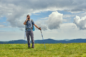 Fototapeta premium Handsome man standing in the meadow and making a call. Mountains on the background. Activity and technology concept.