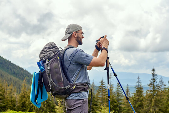 Young bearded traveler standing in a mountain and making a picture by phone. Activity and technology concept.