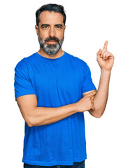 Fototapeta premium Middle aged man with beard wearing casual blue t shirt with a big smile on face, pointing with hand and finger to the side looking at the camera.