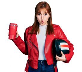 Redhead young woman holding motorcycle helmet and take away coffee making fish face with mouth and squinting eyes, crazy and comical.