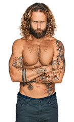 Fototapeta premium Handsome man with beard and long hair standing shirtless showing tattoos skeptic and nervous, disapproving expression on face with crossed arms. negative person.