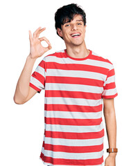 Naklejka premium Handsome hipster young man wearing casual striped t shirt smiling positive doing ok sign with hand and fingers. successful expression.