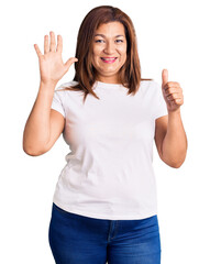 Fototapeta na wymiar Middle age latin woman wearing casual white tshirt showing and pointing up with fingers number six while smiling confident and happy.