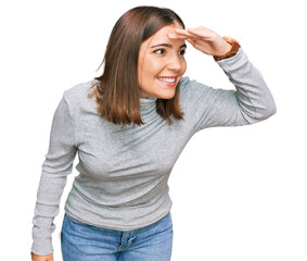 Fototapeta premium Young beautiful woman wearing casual turtleneck sweater very happy and smiling looking far away with hand over head. searching concept.