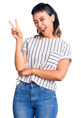 Young woman wearing casual clothes smiling with happy face winking at the camera doing victory sign with fingers. number two.