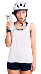 Beautiful young woman with short hair wearing bike helmet and holding water bottle scared and amazed with open mouth for surprise, disbelief face