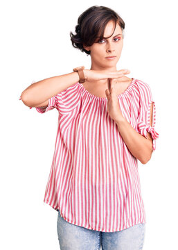 Beautiful young woman with short hair wearing casual summer clothes doing time out gesture with hands, frustrated and serious face