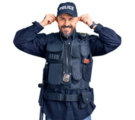 Young handsome man wearing police uniform smiling pulling ears with fingers, funny gesture. audition problem