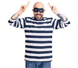 Naklejka premium Young handsome man wearing burglar mask smiling amazed and surprised and pointing up with fingers and raised arms.