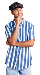 Young hispanic man wearing casual clothes looking confident at the camera smiling with crossed arms and hand raised on chin. thinking positive.