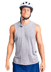 Young handsome man wearing bike helmet relaxed with serious expression on face. simple and natural looking at the camera.