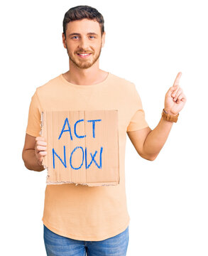 Handsome young man with bear holding act now banner surprised with an idea or question pointing finger with happy face, number one