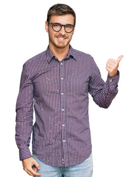 Handsome caucasian man wearing casual clothes and glasses smiling with happy face looking and pointing to the side with thumb up.