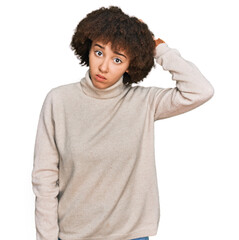 Young hispanic girl wearing wool winter sweater confuse and wondering about question. uncertain with doubt, thinking with hand on head. pensive concept.