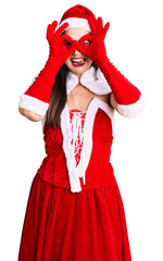 Young beautiful caucasian woman wearing santa claus costume doing ok gesture like binoculars sticking tongue out, eyes looking through fingers. crazy expression.