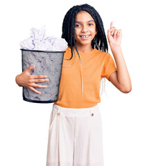 Cute african american girl holding paper bin full of crumpled papers surprised with an idea or question pointing finger with happy face, number one