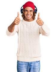 Young hispanic man listening to music using headphones approving doing positive gesture with hand, thumbs up smiling and happy for success. winner gesture.