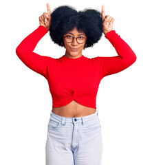 Young african american girl wearing casual clothes and glasses doing funny gesture with finger over head as bull horns