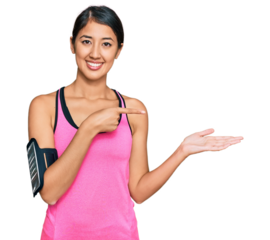 Beautiful asian young sport woman wearing sportswear and arm band amazed and smiling to the camera while presenting with hand and pointing with finger.
