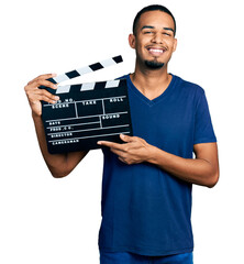 Young african american man holding video film clapboard looking positive and happy standing and...