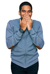 Young handsome hispanic man wearing casual sweatshirt laughing and embarrassed giggle covering...