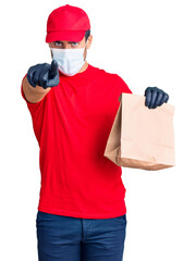 Fototapeta na wymiar Young hispanic man delivering food wearing covid-19 safety mask holding paper bag pointing with finger to the camera and to you, confident gesture looking serious