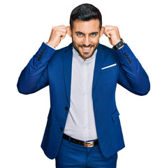 Young hispanic man wearing business jacket smiling pulling ears with fingers, funny gesture. audition problem
