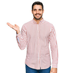 Young hispanic man wearing business shirt smiling cheerful presenting and pointing with palm of hand looking at the camera.