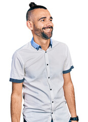 Hispanic man with ponytail wearing casual white shirt looking away to side with smile on face, natural expression. laughing confident.